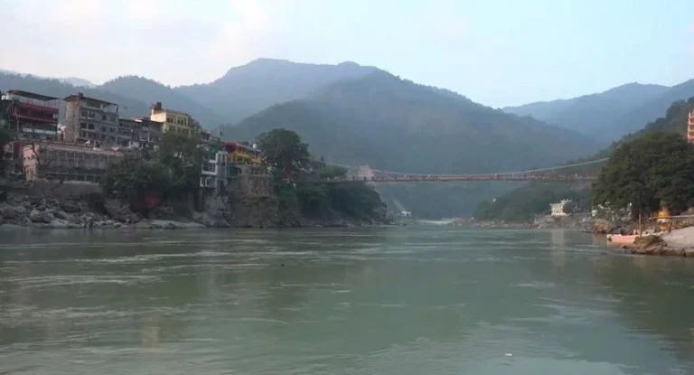 Scenic view of Rishikesh ghats along the Ganges River with temples and the Lakshman Jhula suspension bridge in the background